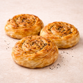 Three puff gul boregi with black seeds on a beige surface
