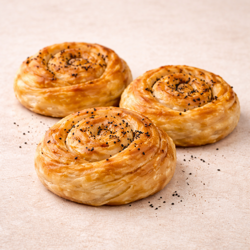 Three puff gul boregi with black seeds on a beige surface