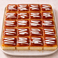 Square tray of caramel-glazed Tres Leches with white drizzle on a beige background