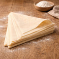 Stack of fresh daily triangle yufka sheets on a wooden surface with flour.