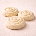 Three uncooked gul boregi rolls on a light pink surface